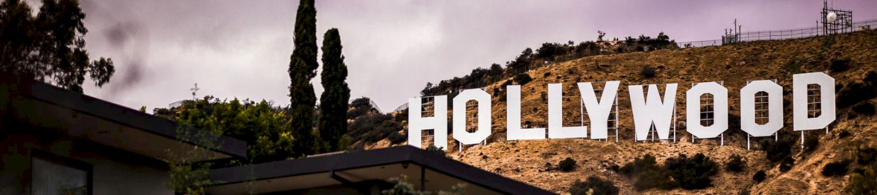 The famous Hollywood sign on a hill, dark clouds above, with foreground buildings.