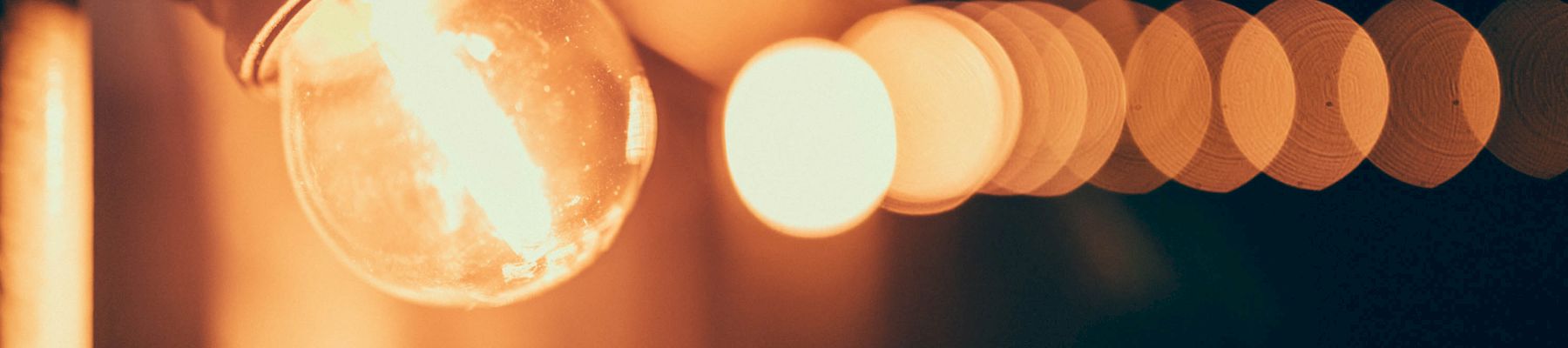 The image shows a close-up of a glowing light bulb with several blurred, illuminated bulbs in a line, creating a bokeh effect in the background.