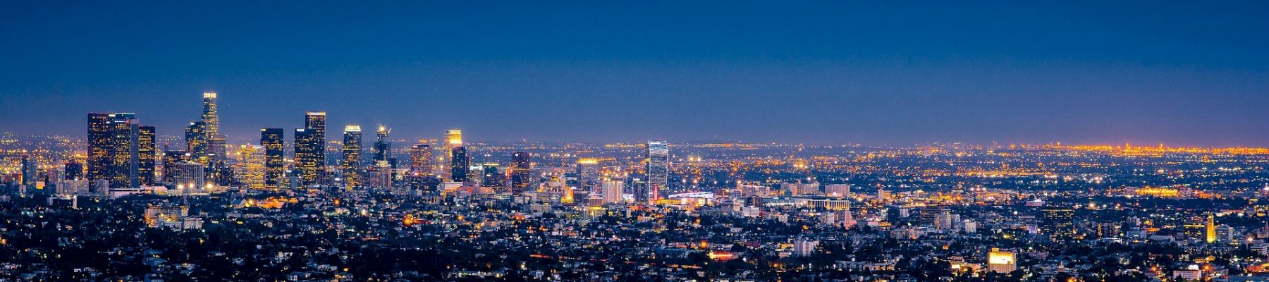 An urban skyline at dusk, showcasing a cityscape with lit buildings, streetlights, and a transitioning sky from blue to night.